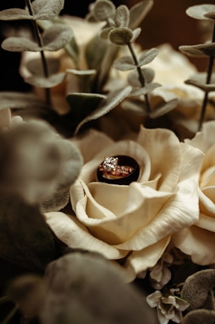 A close-up of a wedding ring resting on a bouquet of flowers.