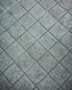 A textured, grey tiled surface with a repeated diamond pattern. The tiles appear to be made of stone or concrete and have a rough, weathered look.
