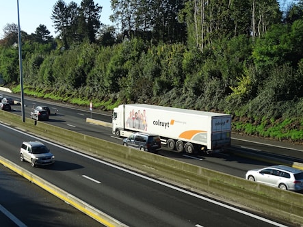 A large cargo truck driving on a highway surrounded by green fields under a clear blue sky.