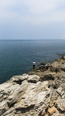 An instructor demonstrating bottom fishing techniques by a rocky shoreline.