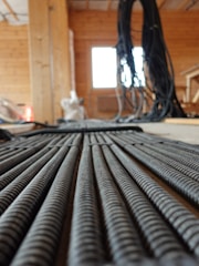 A close-up view of coiled cables neatly laid out on a wooden floor inside a construction site. In the background, there are more cables hanging and an unfinished wooden structure, indicating an indoor construction or renovation setting.