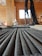 A close-up view of coiled cables neatly laid out on a wooden floor inside a construction site. In the background, there are more cables hanging and an unfinished wooden structure, indicating an indoor construction or renovation setting.