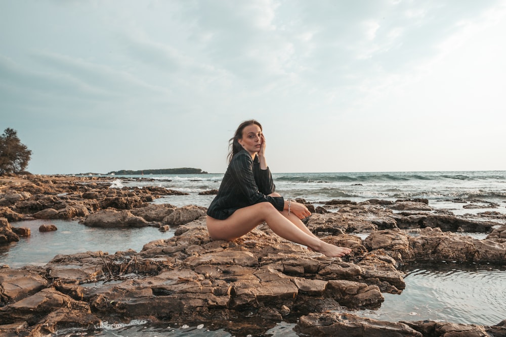woman in black dress sitting on brown rock near sea during daytime