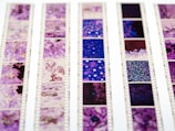 Rows of photographic film negatives with intricate, colorful patterns in shades of purple and blue. The film strips are aligned vertically with visible perforations and frame numbers.