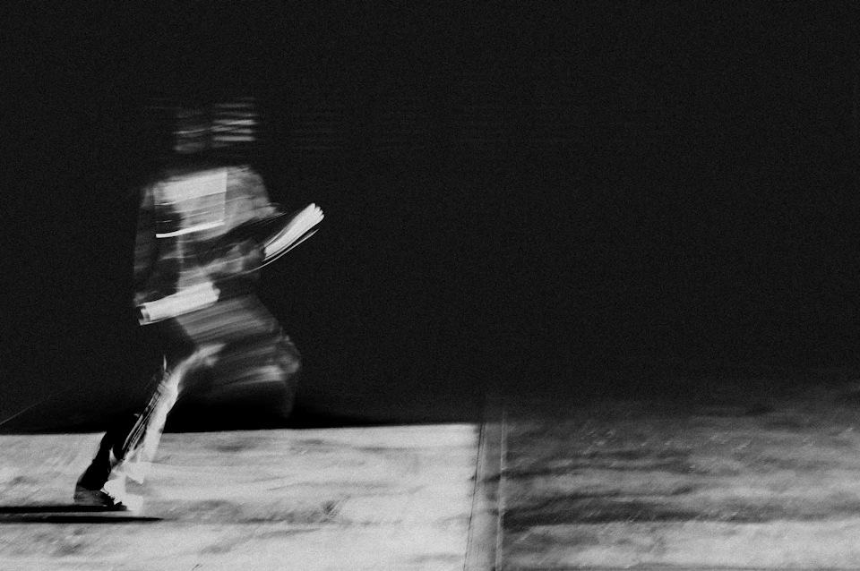 Person runs on sidewalk wearing black and white outfit, holding a book in hand