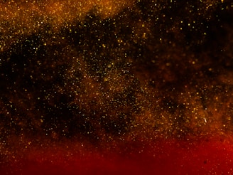 A cosmic scene with a dense distribution of golden and red particles resembling a starry night or galaxy. Light and shadow create a deep, immersive effect.