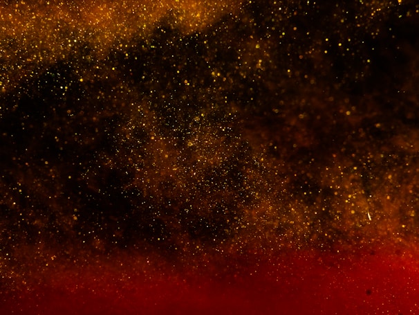 A cosmic scene with a dense distribution of golden and red particles resembling a starry night or galaxy. Light and shadow create a deep, immersive effect.