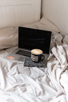 black and silver laptop computer on white bed