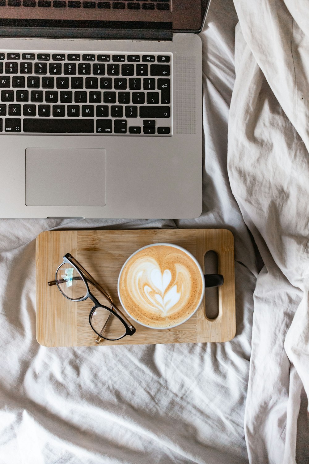 black and silver laptop computer beside black framed eyeglasses on white textile