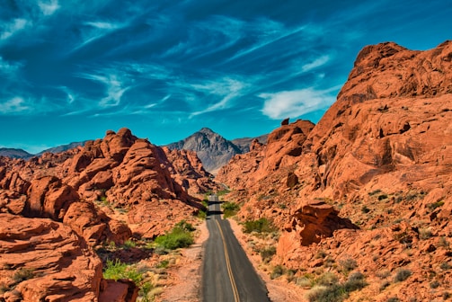 gray asphalt road between brown rocky mountains under blue sky during daytime