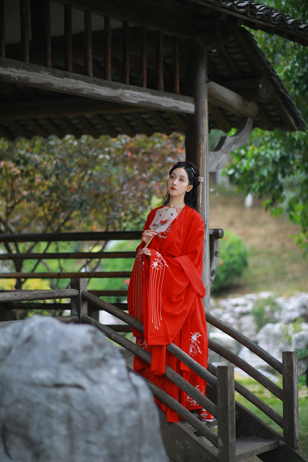 woman in red and white sari standing near brown wooden gazebo during daytime
