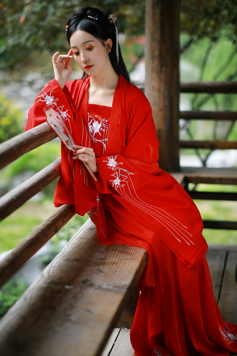 woman in red and white floral kimono sitting on brown wooden bench during daytime