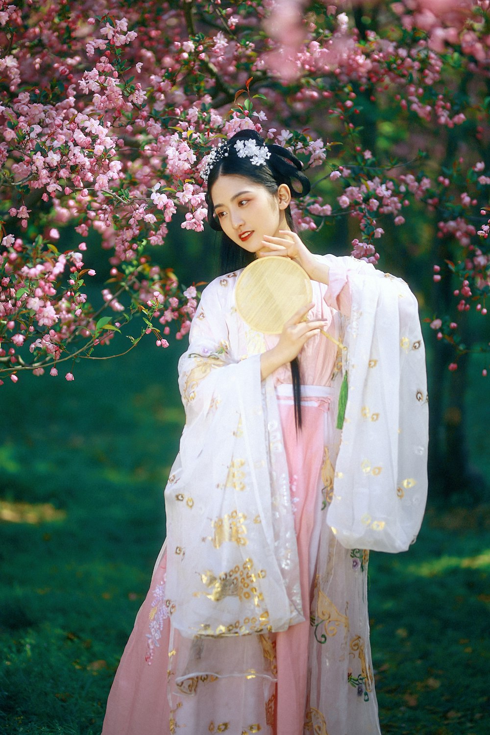 Femme en robe fleurie jaune et blanche debout près de fleurs roses pendant la journée