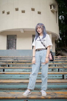 woman in white t-shirt and blue denim jeans standing on brown wooden bench during daytime