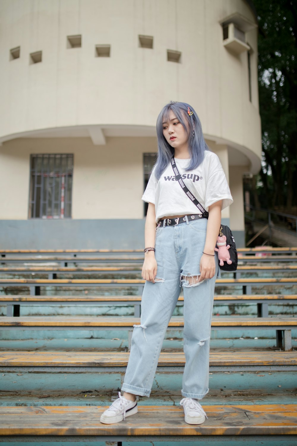 woman in white t-shirt and blue denim jeans standing on brown wooden bench during daytime