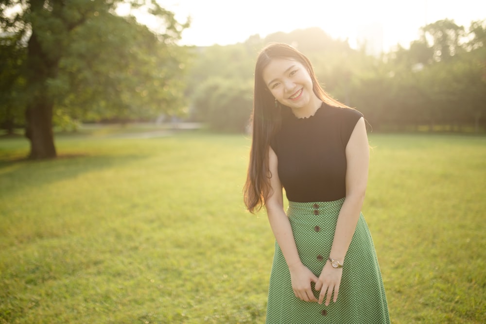 woman in black tank top and green and white checked skirt standing on green grass field