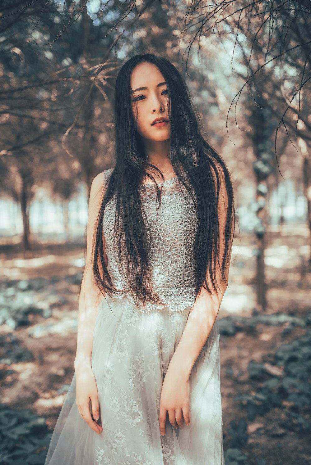 woman in white dress standing near bare trees during daytime