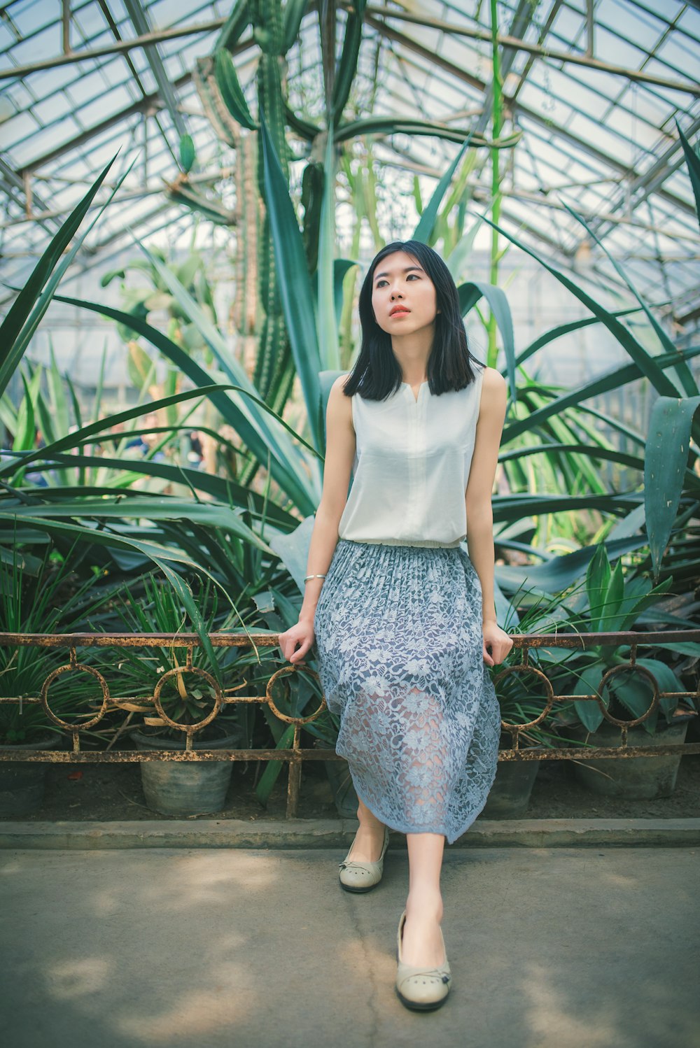 woman in white tank top and blue and white floral skirt standing on brown wooden bridge