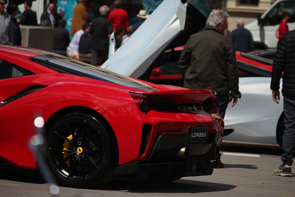 man in black suit standing beside red ferrari