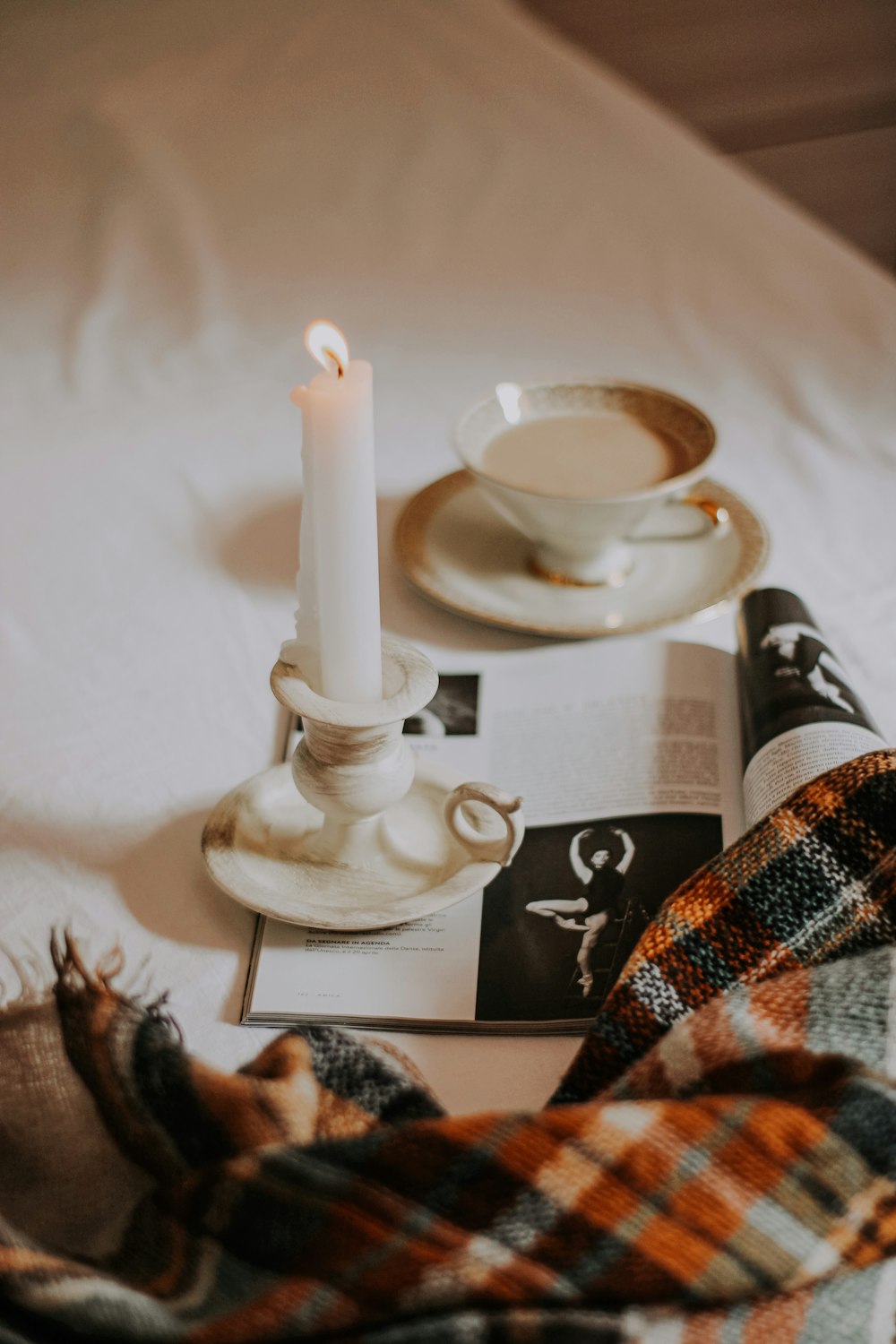 white ceramic cup on white ceramic saucer beside white candle holder