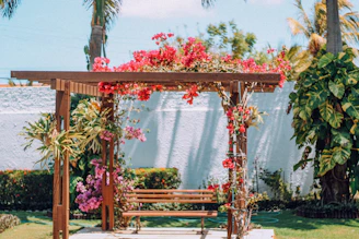A cozy wooden pergola nestled in a sunlit European garden with climbing vines and comfortable seating underneath.