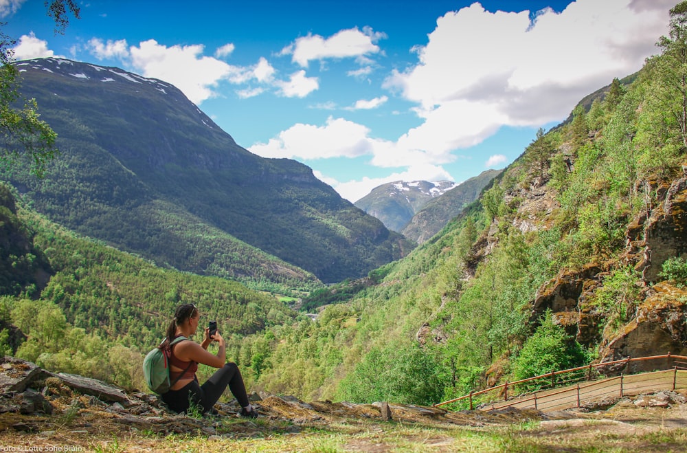 woman in gray tank top sitting on brown rock near green mountains during daytime