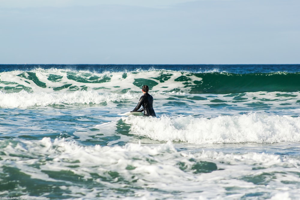 person in black wet suit surfing on sea waves during daytime