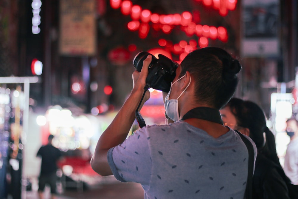 man in white t-shirt using black dslr camera