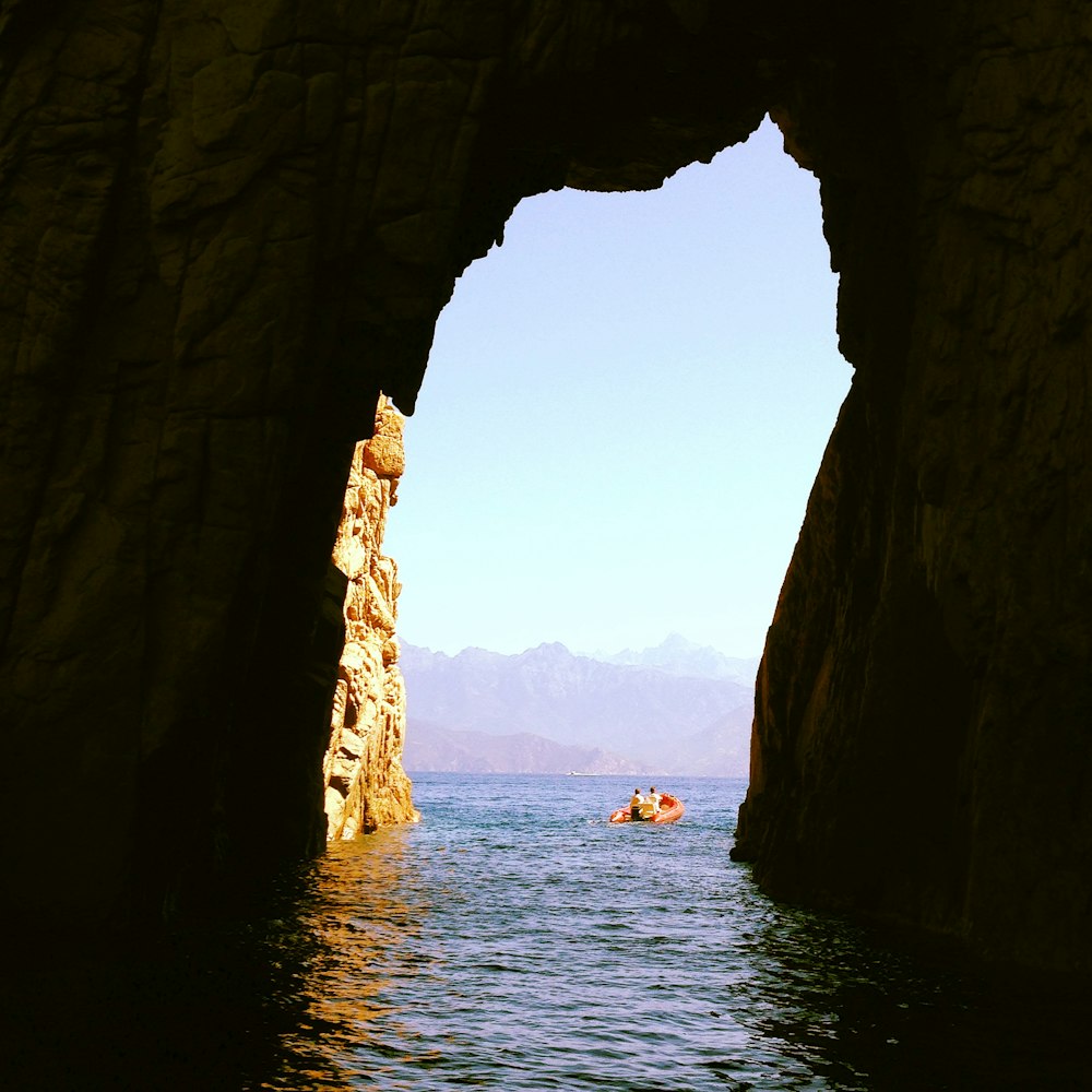 people riding boat on sea near brown rock formation during daytime