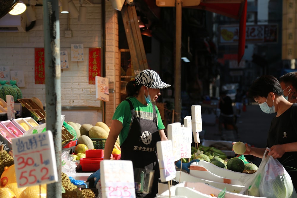 woman in green and black shirt standing in front of vegetable stand
