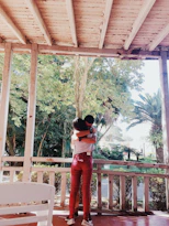 woman in red pants standing on brown wooden porch during daytime