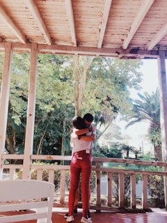 woman in red pants standing on brown wooden porch during daytime