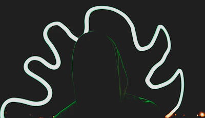 Close-up of a black hoodie featuring a mysterious monochrome silhouette print under soft neon lighting
