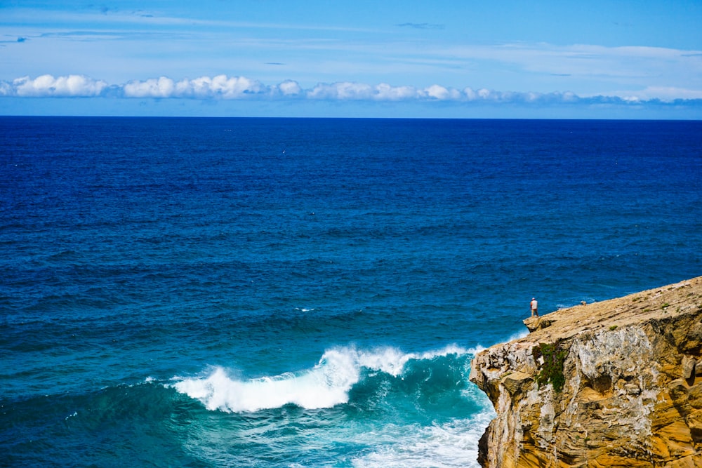 person standing on rock formation near sea during daytime