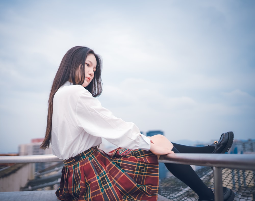 woman in white long sleeve shirt and red and black plaid skirt standing beside railings