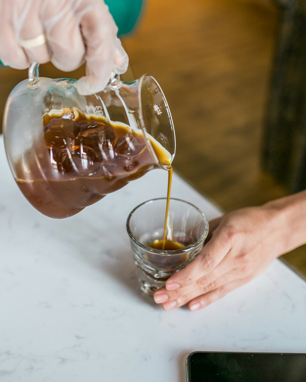 person pouring brown liquid on clear drinking glass