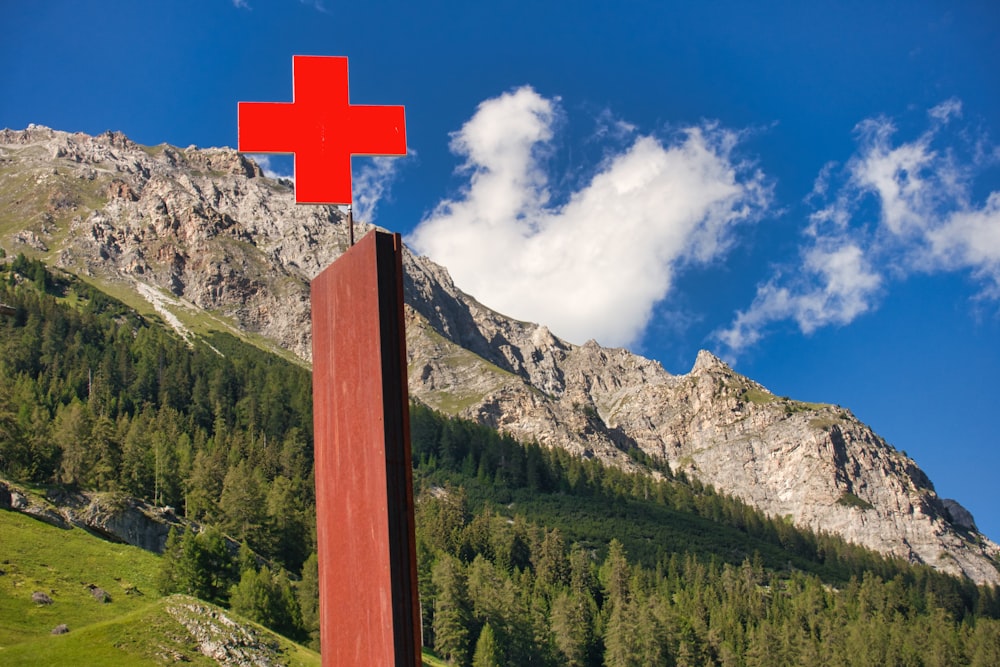 Braunes Holzkreuz auf grünem Grasfeld in Bergnähe unter blau-weißem bewölktem Himmel während