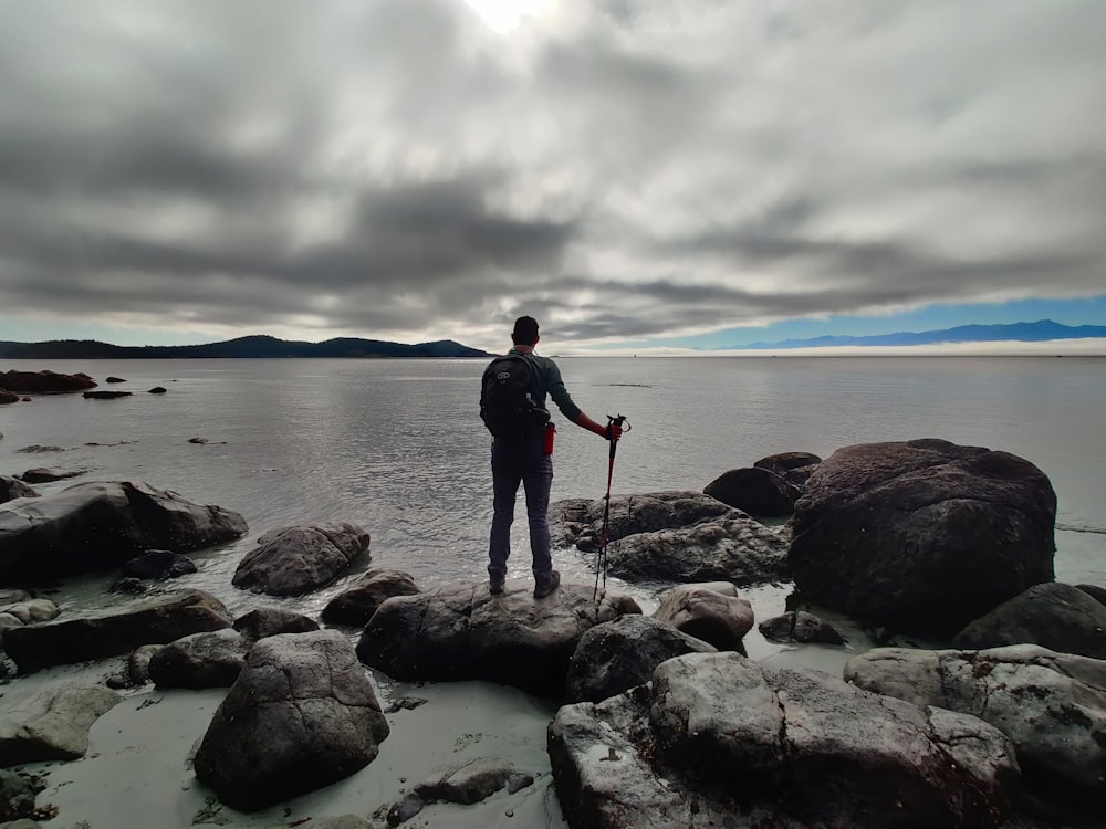 man in black jacket standing on rocky shore during daytime