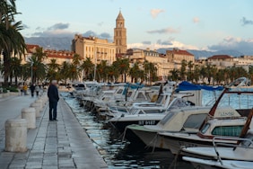 man in black jacket walking on dock near white and blue boats during daytime