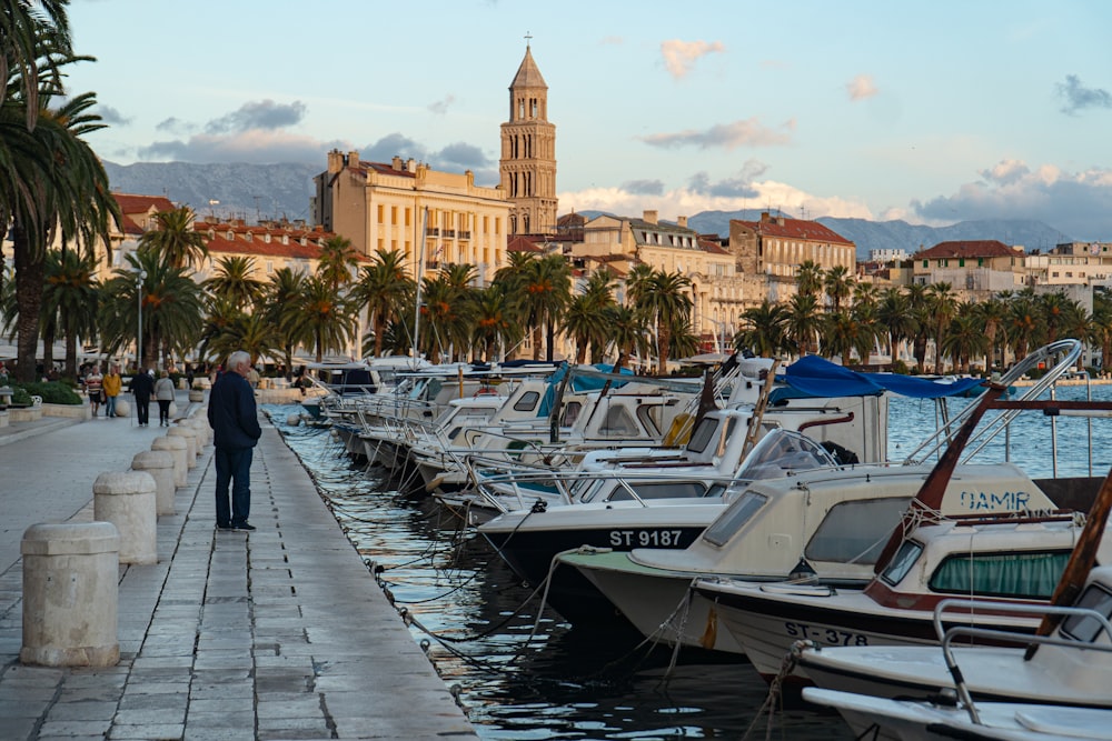 Homme en veste noire marchant sur le quai près des bateaux blancs et bleus pendant la journée