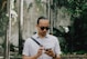 man in white button up shirt wearing black sunglasses holding black smartphone