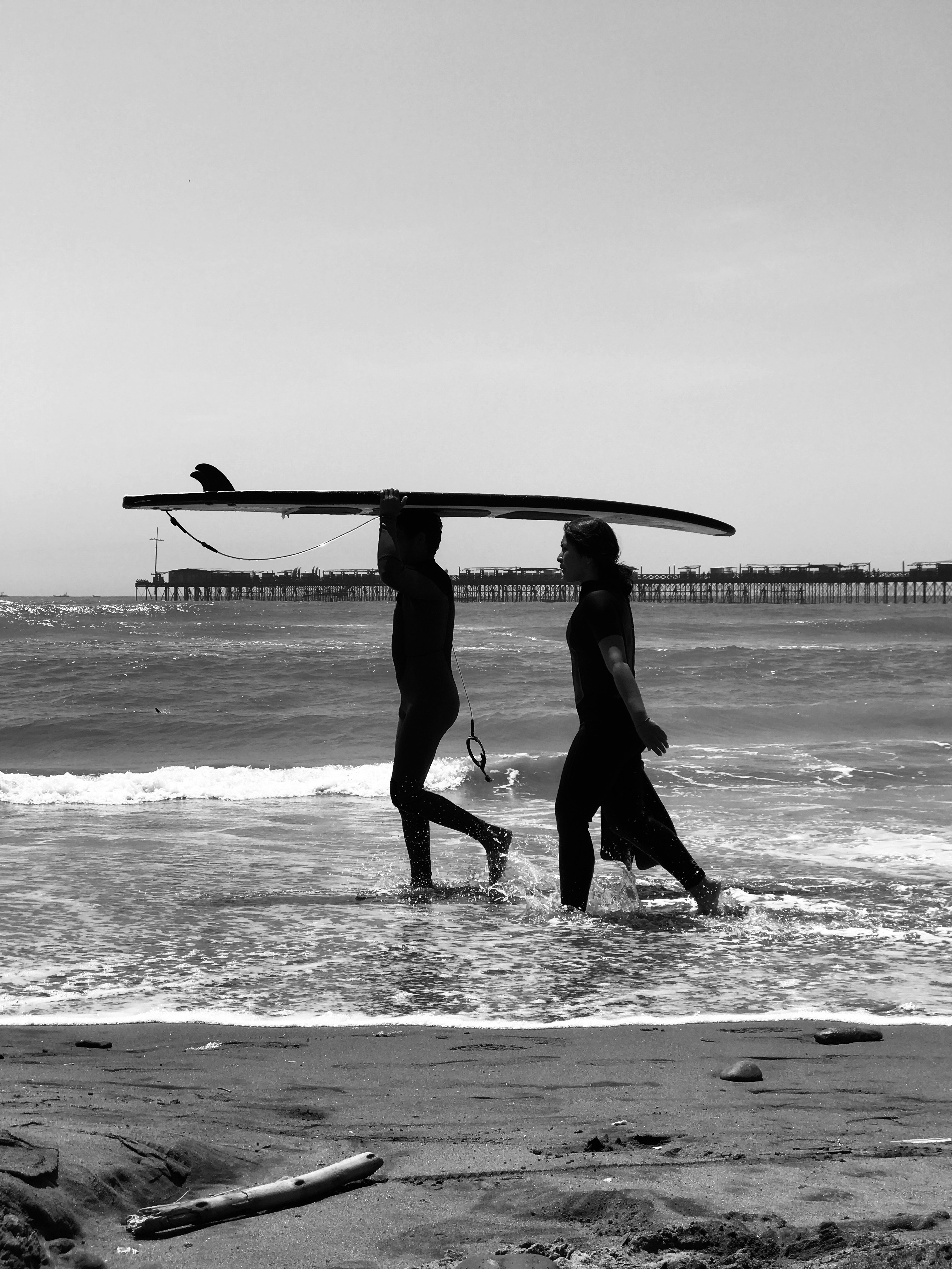 grayscale photo of 2 women holding surfboard on beach