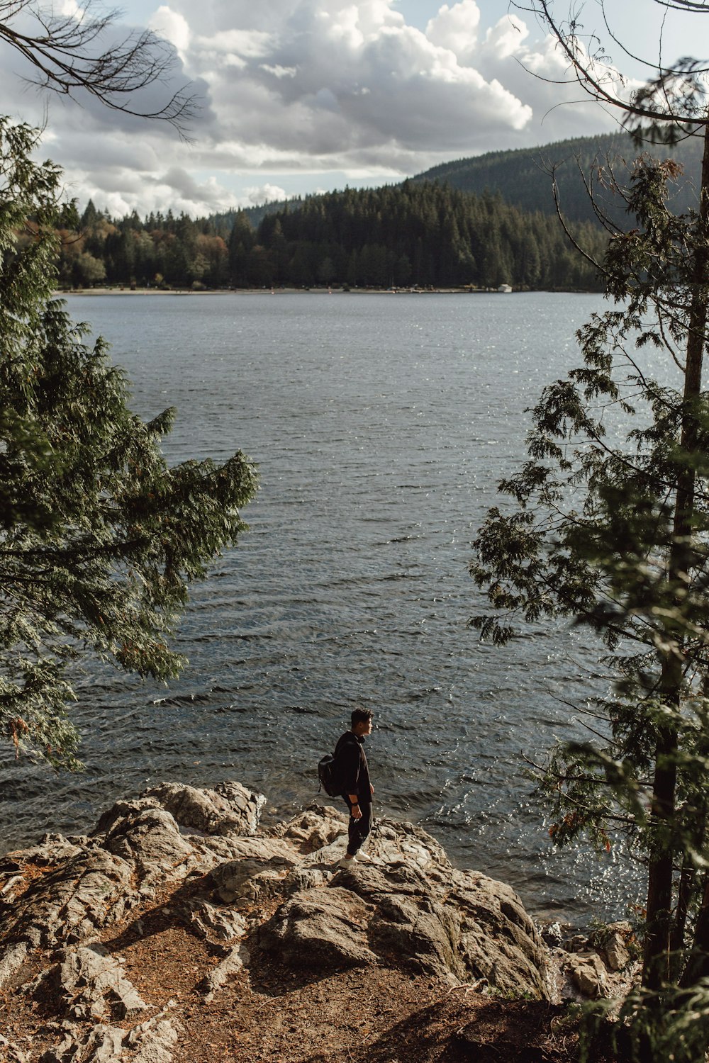 pessoa em jaqueta preta em pé na rocha perto do corpo de água durante o dia