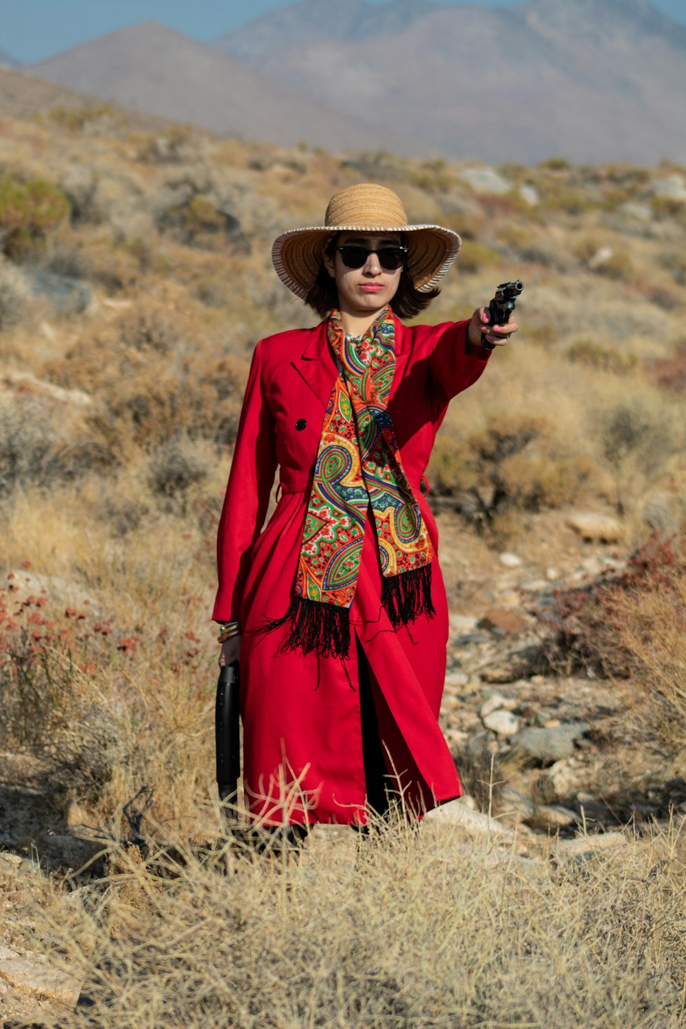 茶色の草の上に立つ茶色の太陽の帽子をかぶった赤と黒の長袖ドレスを着た女性