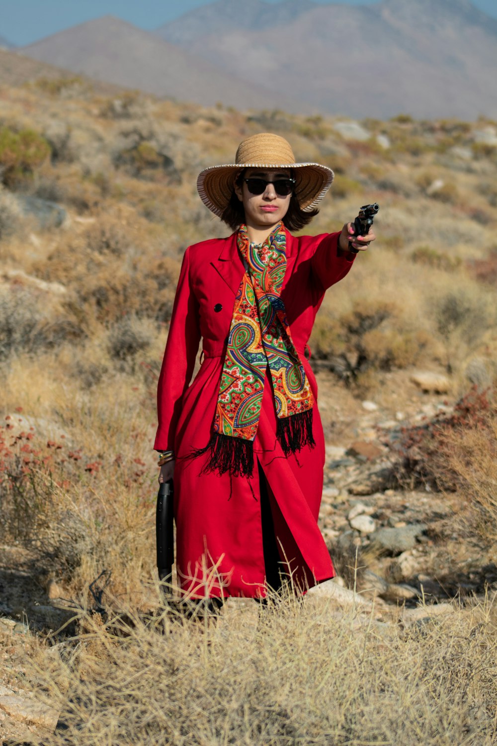 Frau in rot-schwarzem langärmeligem Kleid mit braunem Sonnenhut auf braunem Gras stehend