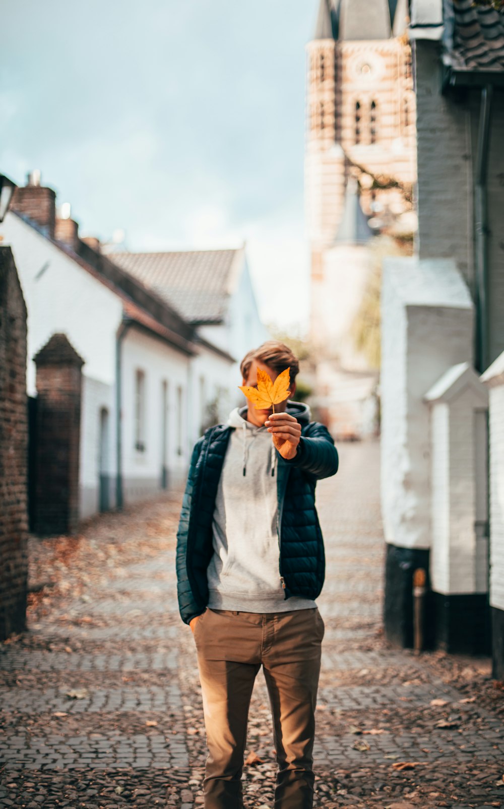 man in blue jacket and brown pants standing beside brick wall during daytime