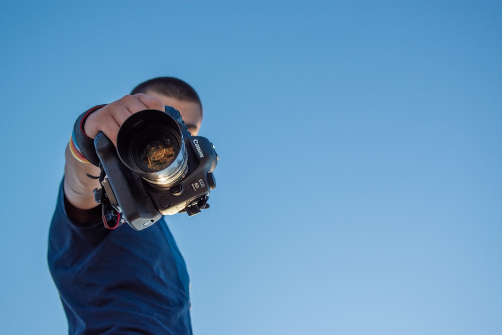 man in blue shirt holding black dslr camera