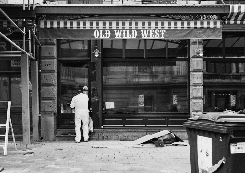 man in white long sleeve shirt and pants walking on sidewalk in grayscale photography