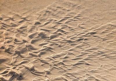 Fine sand displays intricate patterns shaped by the wind, with smooth ripples and lines creating a natural texture. The surface has varying shades from light to slightly darker sand tones.