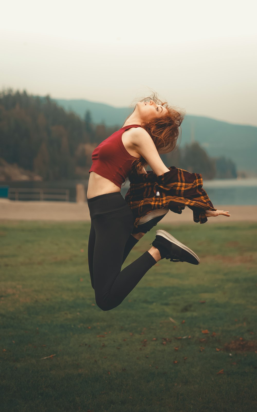 woman in red shirt and black pants jumping on green grass field during daytime